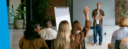 Man presenting at a learning seminar with participants hands raised. 